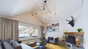 Un salon moderne avec une cheminée, une grande fenêtre et un lustre.