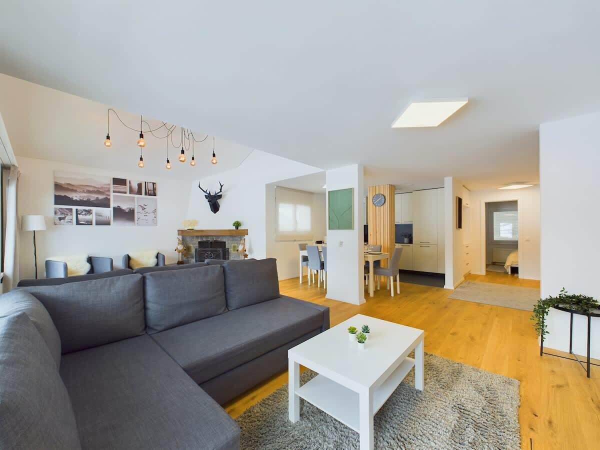 Ein modernes Wohnzimmer mit einem grauen Sofa, einem weißen Couchtisch und einem Essbereich im Hintergrund.