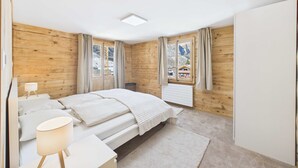 A bedroom with wooden walls, a bed, a bedside table with a lamp, and a view of mountains through the window.