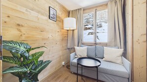 Una habitación acogedora con paredes de madera, un sofá, una mesita, una lámpara y una ventana con vistas a un paisaje nevado.