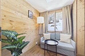 Una habitació acollidora amb parets de fusta, un sofà, una taula petita, una làmpada i una finestra amb vista a un paisatge nevado.