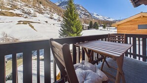 A wooden deck with a table and chairs, overlooking a snowy landscape with mountains in the background.