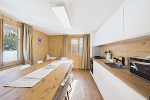Une cuisine moderne avec une table en bois, des armoires blanches et une vue par la fenêtre.
