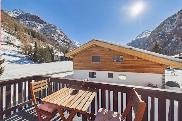 A wooden cabin with a balcony, a wooden table, and chairs.