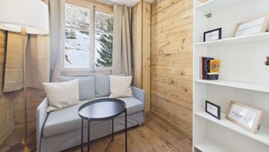 A cozy room with a wooden wall, a grey sofa, a small round table, and a bookshelf with framed items.