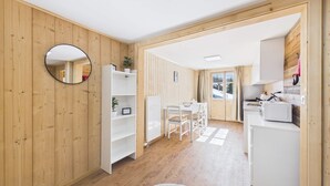 Moderni sisustus, jossa on puuseinät, valkoinen ruokailutila, valkoisilla kodinkoneilla varustettu keittiö ja suuri peili.