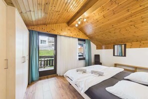 Quarto com teto de madeira, uma cama grande, uma televisão e uma varanda com cortinas.