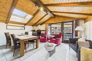 Um quarto espaçoso com teto de madeira, uma mesa de jantar, cadeiras, um sofá e uma varanda com vista.
