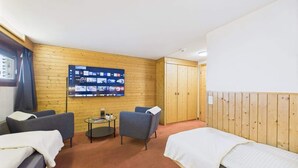 Habitación de hotel con dos camas, un televisor montado en la pared, una mesita pequeña y un panel de pared de madera.