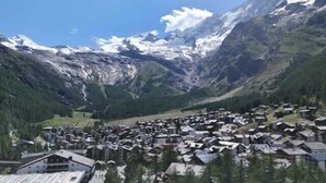 Un pueblo en la montaña con casas, un telesilla y picos nevados.