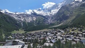 Een bergdorpslandschap met huizen, een skilift en besneeuwde bergtoppen.