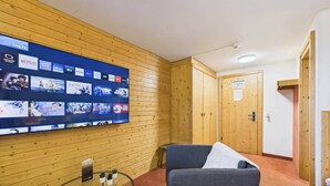 Una habitación con una TV empotrada que muestra diferentes servicios de streaming, un sofá gris y una puerta de madera.