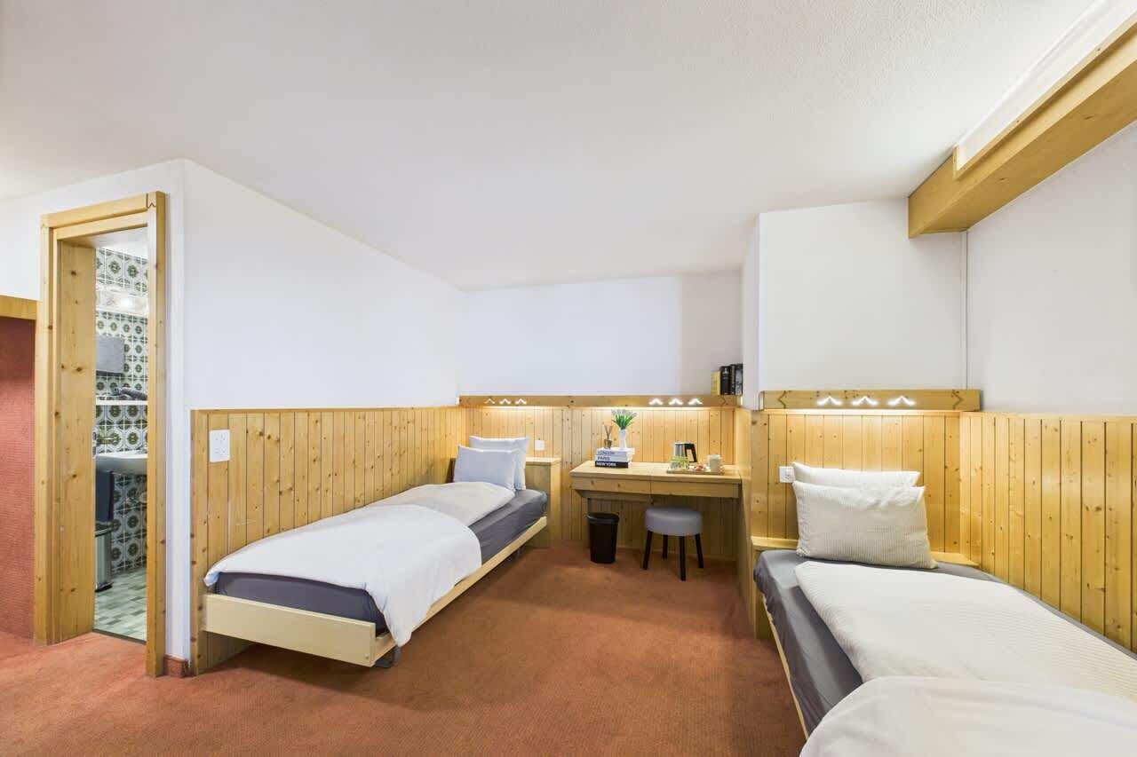 Ein Zimmer mit zwei Betten, einem Schreibtisch und einem kleinen Hocker.
