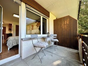 Un balcon avec deux chaises et une table, une porte en bois et une fenêtre.