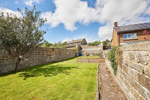 A courtyard with a stone wall, a tree, and a house with solar panels. - Host & Stay | The Mews (Rothbury)