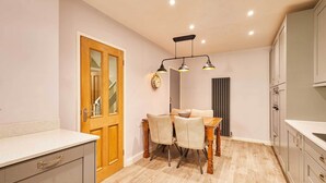 A kitchen with a dining table, chairs, a clock, and cabinets. - Host & Stay | The Mews (Rothbury)