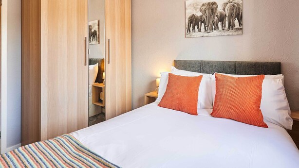 A hotel room with a bed, a nightstand, a wall-mounted picture of elephants, and a wooden wardrobe. - Host & Stay | The Mews (Rothbury)