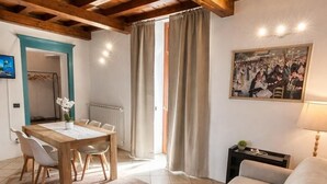 A living room with a sofa, a dining table with chairs, a painting on the wall, and a window with curtains. - Casa Renoir: A bright one-bedroom apartment in the historic center of Suna, near the lake and the beach  (Suna)