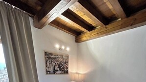 A bedroom with a bed, a nightstand, a lamp, a painting, and a window with curtains. - Casa Renoir: A bright one-bedroom apartment in the historic center of Suna, near the lake and the beach  (Suna)