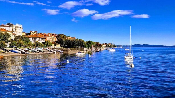 A waterfront with boats, a marina, and buildings along the shore. - Casa Renoir: A bright one-bedroom apartment in the historic center of Suna, near the lake and the beach  (Suna)