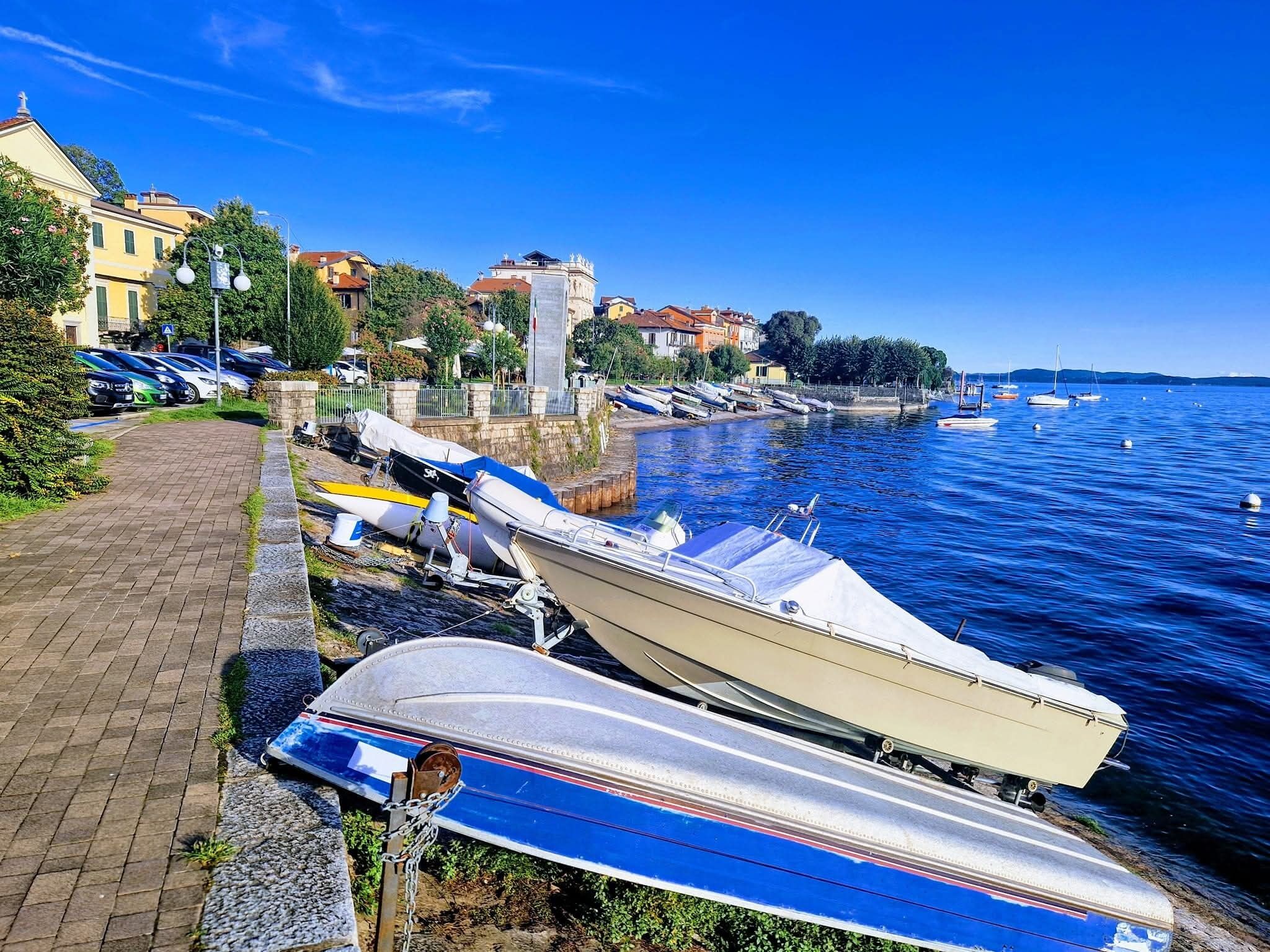 A waterfront with boats docked, a paved walkway, and buildings in the background.