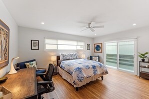 A bedroom with a bed, desk, chairs, and a ceiling fan.