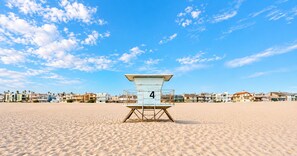 A lifeguard tower labeled '4' on a sandy beach with a row of houses in the background.