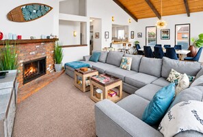 A living room with a fireplace, a grey sofa, and a dining area with blue chairs.