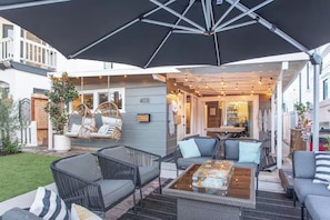 Eine Terrasse im Freien mit Korbmöbeln, einem Glastisch und einem großen Sonnenschirm.