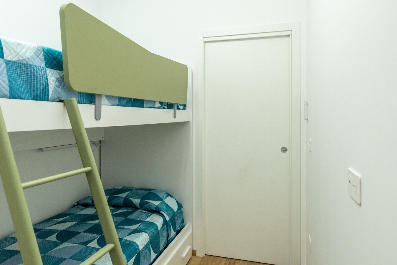 A bunk bed with a ladder, a door, and a power outlet on the wall.