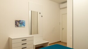 Un dormitorio con cama, cómoda, espejo, puerta y una obra de arte colgada en la pared.