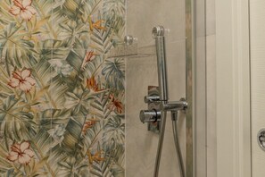 Une douche avec des accessoires chromés et un mur recouvert de carreaux à motifs floraux.