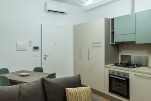 Una cocina compacta con estufa a gas, horno y armarios blancos. Cuenta con un comedor con mesa y sillas.