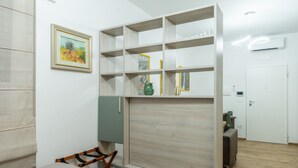 Een kamer met een bed, een groen kastje, een houten plankunit, een lijst met een afbeelding en een deur.