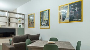 Een moderne woonkamer met een bank, een eettafel en groene stoelen. Er hangen drie kunstwerken in de muur.