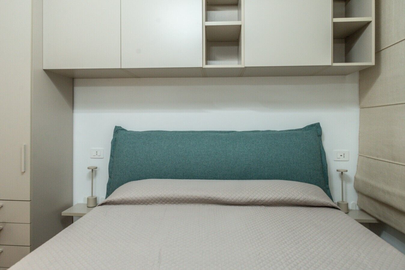 Un letto con una testiera color petrolio, una coperta beige e due comodini con lampade.