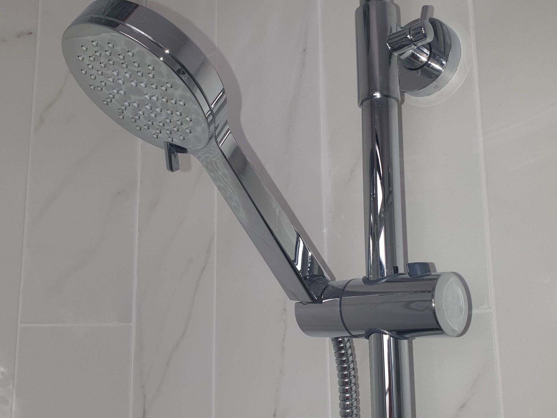 A chrome showerhead with a round, perforated design, attached to a vertical chrome pipe with a flexible hose.