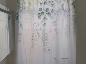 Casa de banho com cortina de chuveiro branca com padrão floral.