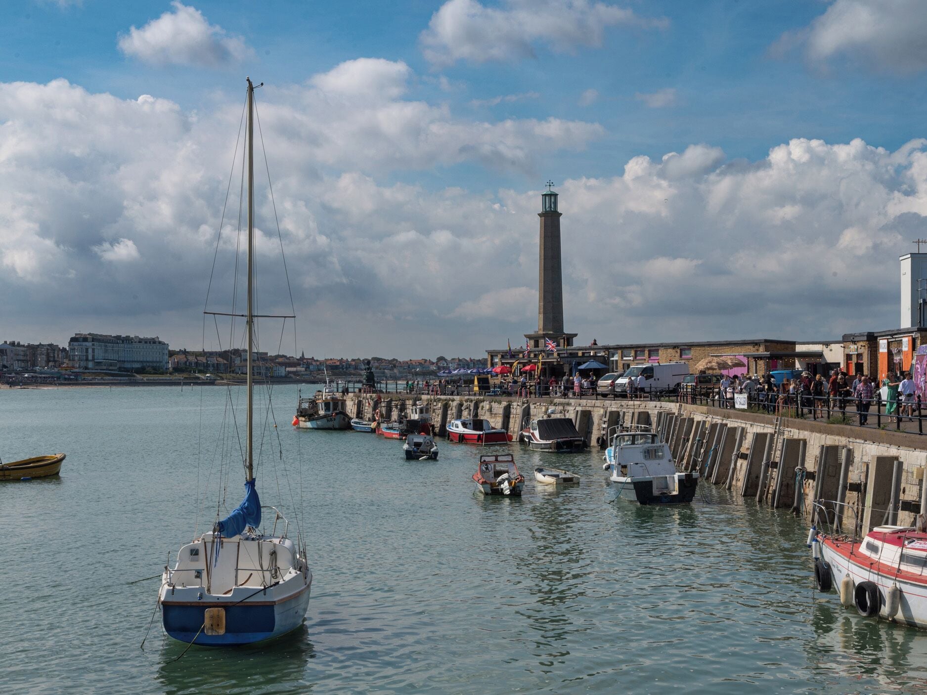 A harbor with boats, a lighthouse, and a pier with people.
