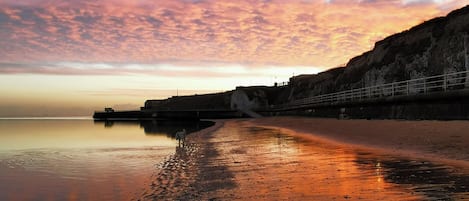 Un paisaje costero con una playa tranquila, un acantilado y un puente.
