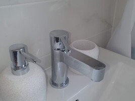 Un lavandino da bagno con un rubinetto cromato, un dispenser di sapone e un porta carta igienica.
