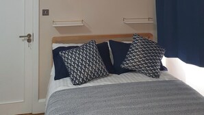 A bedroom with a bed, two bedside tables, a wall-mounted light, and a door. - Kinamara Ensuite Room (Margate)