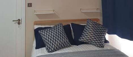 A bedroom with a bed, two bedside tables, a wall-mounted light, and a door.