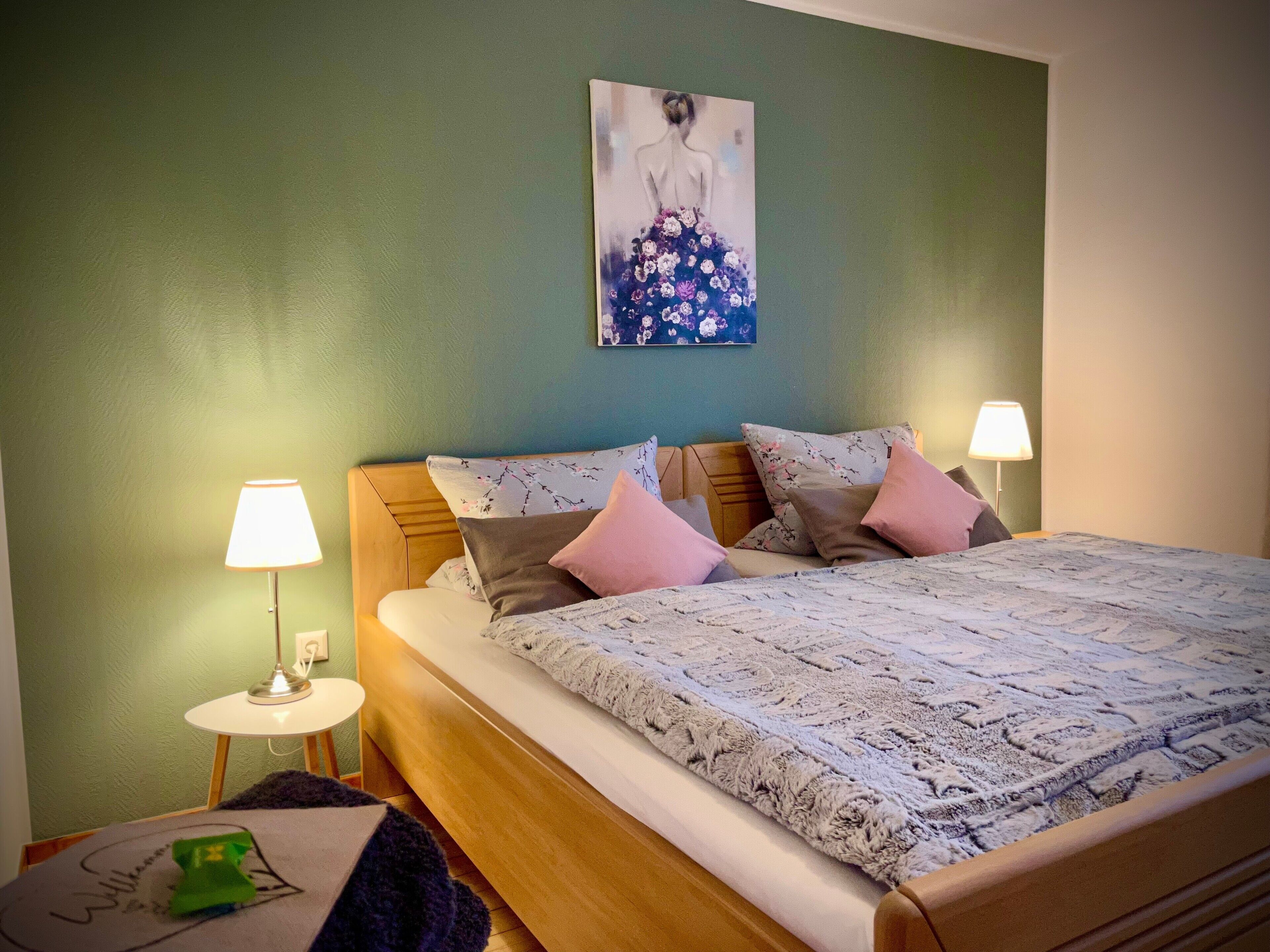 Ein ordentlich bezogenes Bett mit einem gemusterten Überwurf, zwei Nachttischlampen und einem Blumenbild an der Wand.