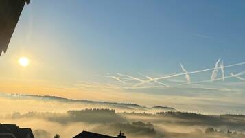 A sunrise over a misty landscape with visible contrails in the sky.