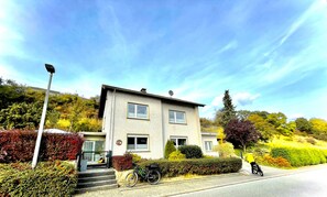 Ein zweistöckiges Gebäude mit flachem Dach und Satellitenschüssel, vor der Tür ein Fahrrad abgestellt.