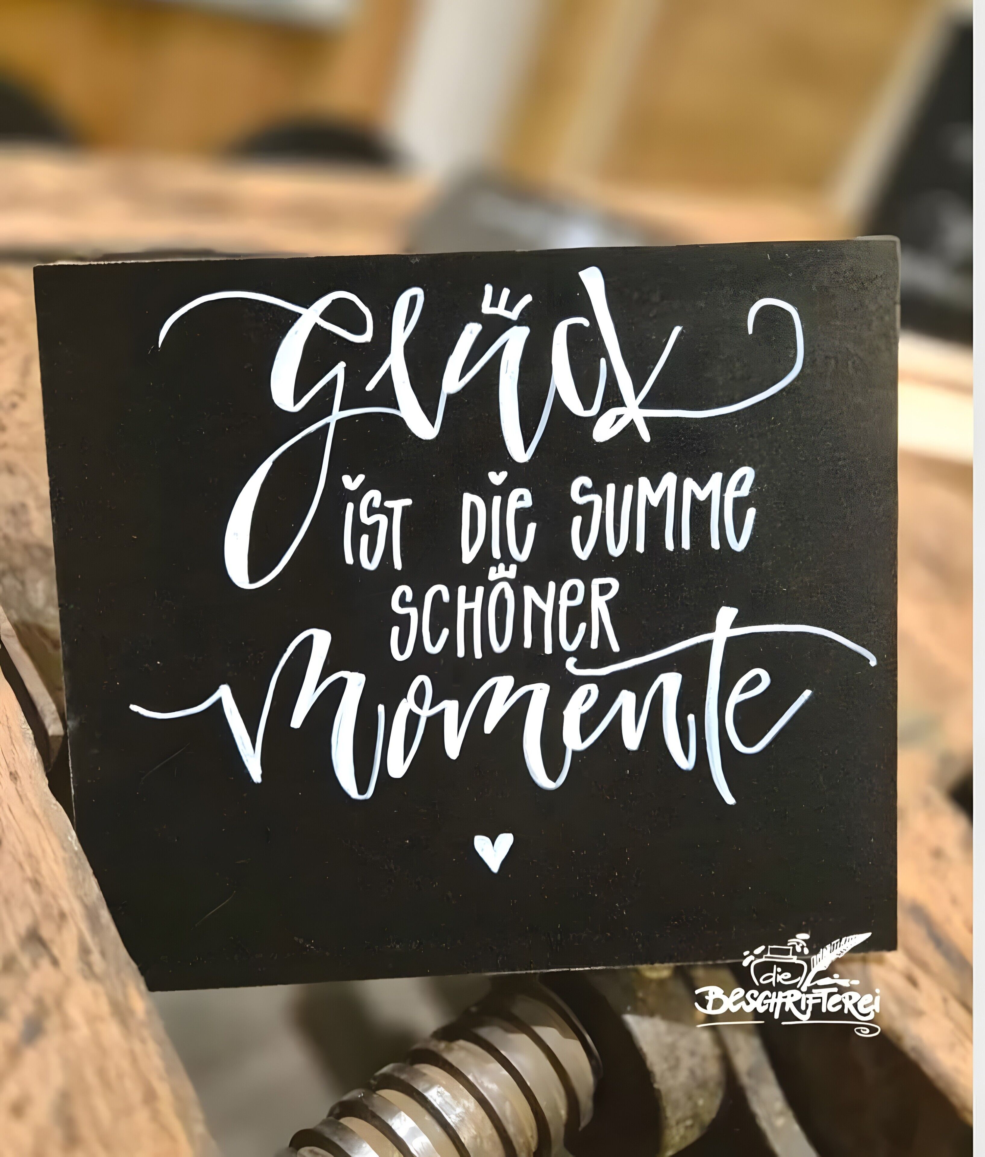 Ein schwarzes Schild mit weißer, geschwungener Schrift und einem kleinen Logo.