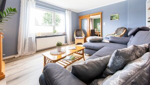 A living room with a sofa, a wooden coffee table, a chair, and a window with curtains.