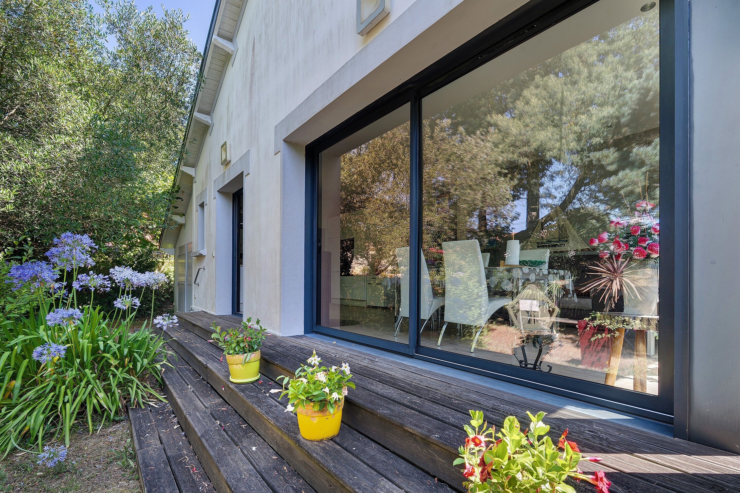 Un edificio moderno con ampie vetrate e un terrazza in legno con piante in vaso.