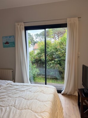A bedroom with a bed, a TV, and a sliding glass door leading to a garden. - Holiday Home 'Aux Jolis Bambous, Garden' with Private Terrace and Garden (Pornic)